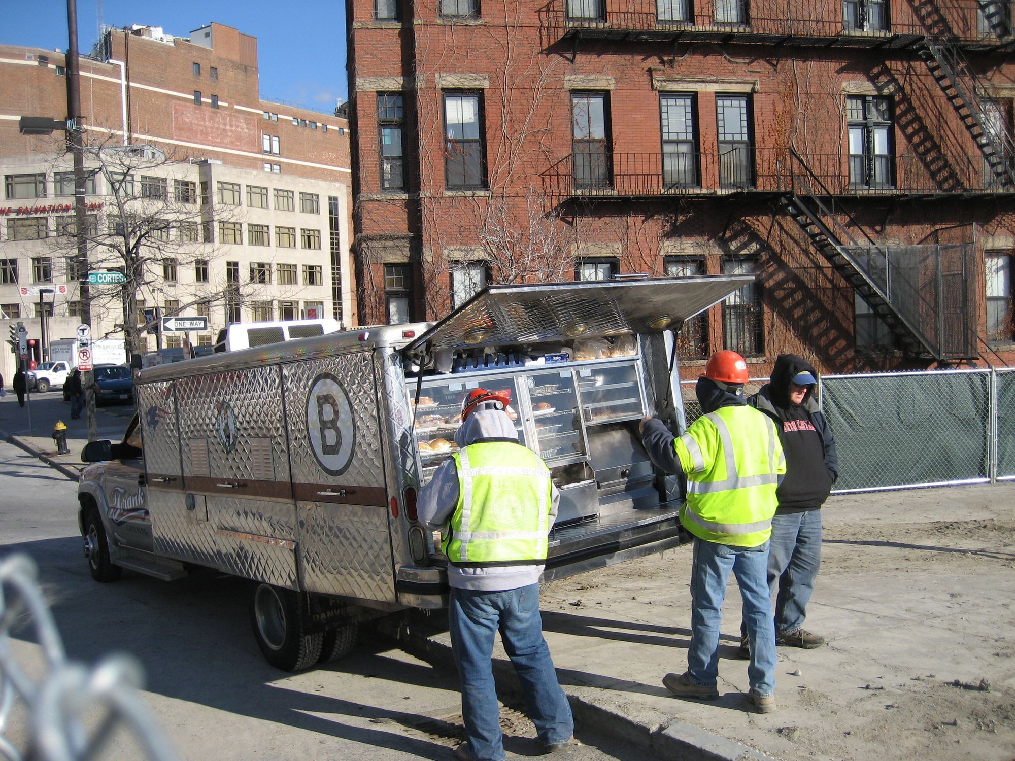 Three workers on a NYC street patronizing a lunch truck. It looks pretty cold out, their hoods are up under their hardhats.