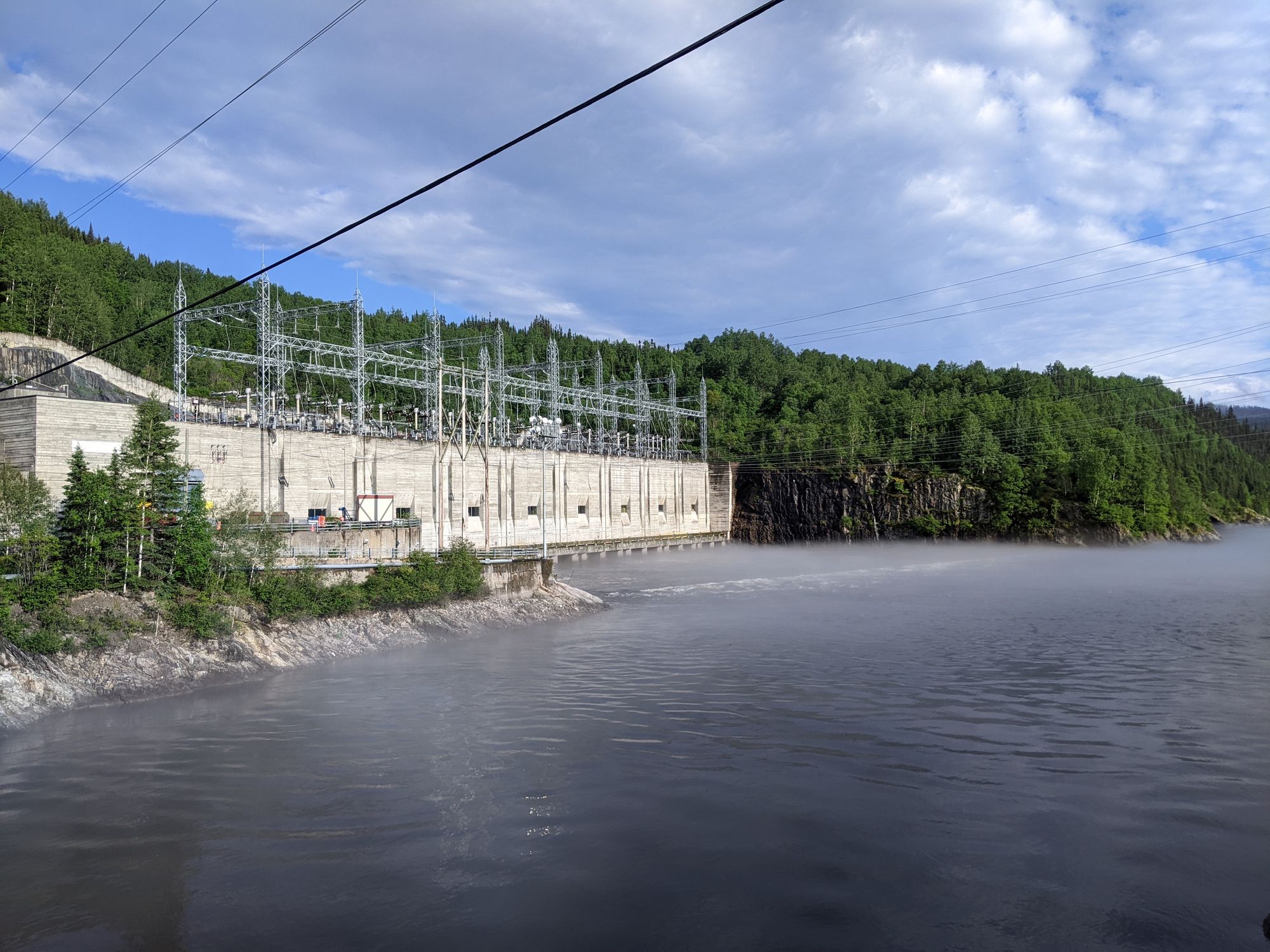 a concrete building with powerlines leading to it at the edge of the water