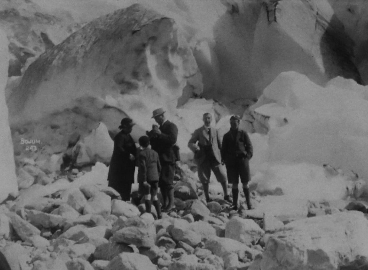 Five people dressed in suits and hats, standing on a glacier
