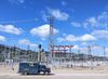 a truck drives in front of open air transformers and powerlines